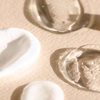 Creamy white and clear gel-like swatches on tan textured surface, showing ingredients in Mirabella foundation