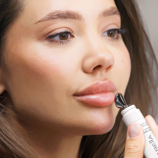 Woman applying Mirabella Beauty lip product for a glossy, hydrated lip look with natural, polished makeup.