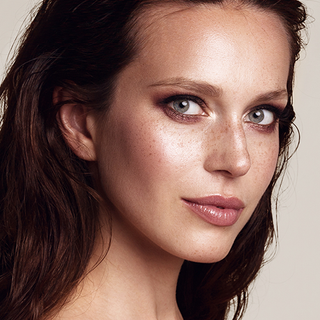 close-up portrait of a woman wearing soft, radiant summer makeup with glowing skin, defined lashes, bronzed cheeks, and a natural nude lip