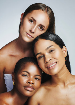 three women with diverse skin tones posing together, showcasing healthy, radiant complexion and natural beauty 