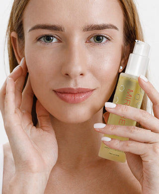 Woman with natural makeup holding Mirabella Skinphony Pro Face Cleanser bottle, lips gently closed, clean skincare beauty portrait