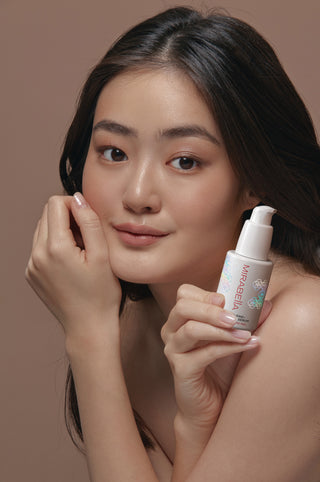 Model with glowing skin holding Mirabella All in 1+ AHA/BHA Clarifying Serum bottle, showcasing clean pro-grade skincare for smooth radiant complexion.