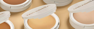Close-up of Mirabella Pure Press powder foundation compacts in different shades arranged on neutral background.