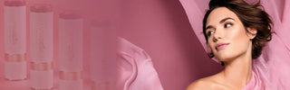 Model wearing Mirabella Soft Satins Lipstick in Pink Quartz with flowing pink satin fabric and lipstick packaging in background.